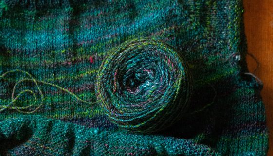 green and teal handspun raglan sweater in progress with yarn cake